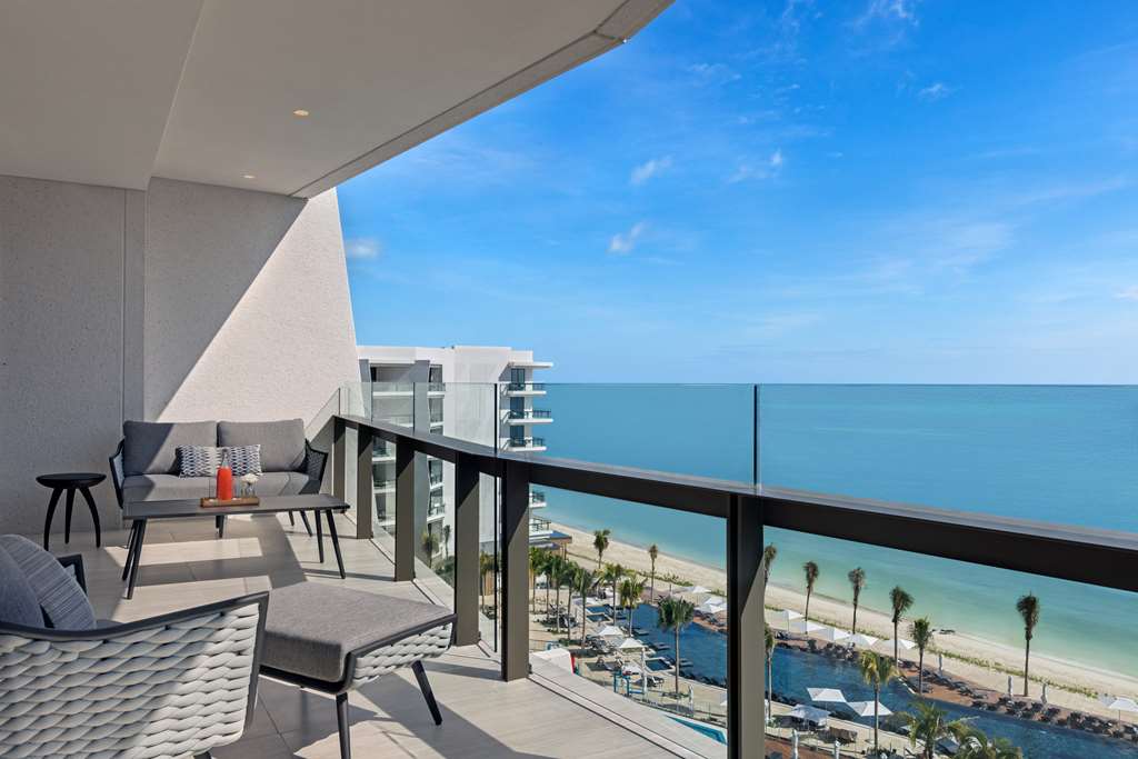 Beachfront balcony with lounge seating, ocean and sand views, palm trees, and resort buildings at Hilton Cancun.