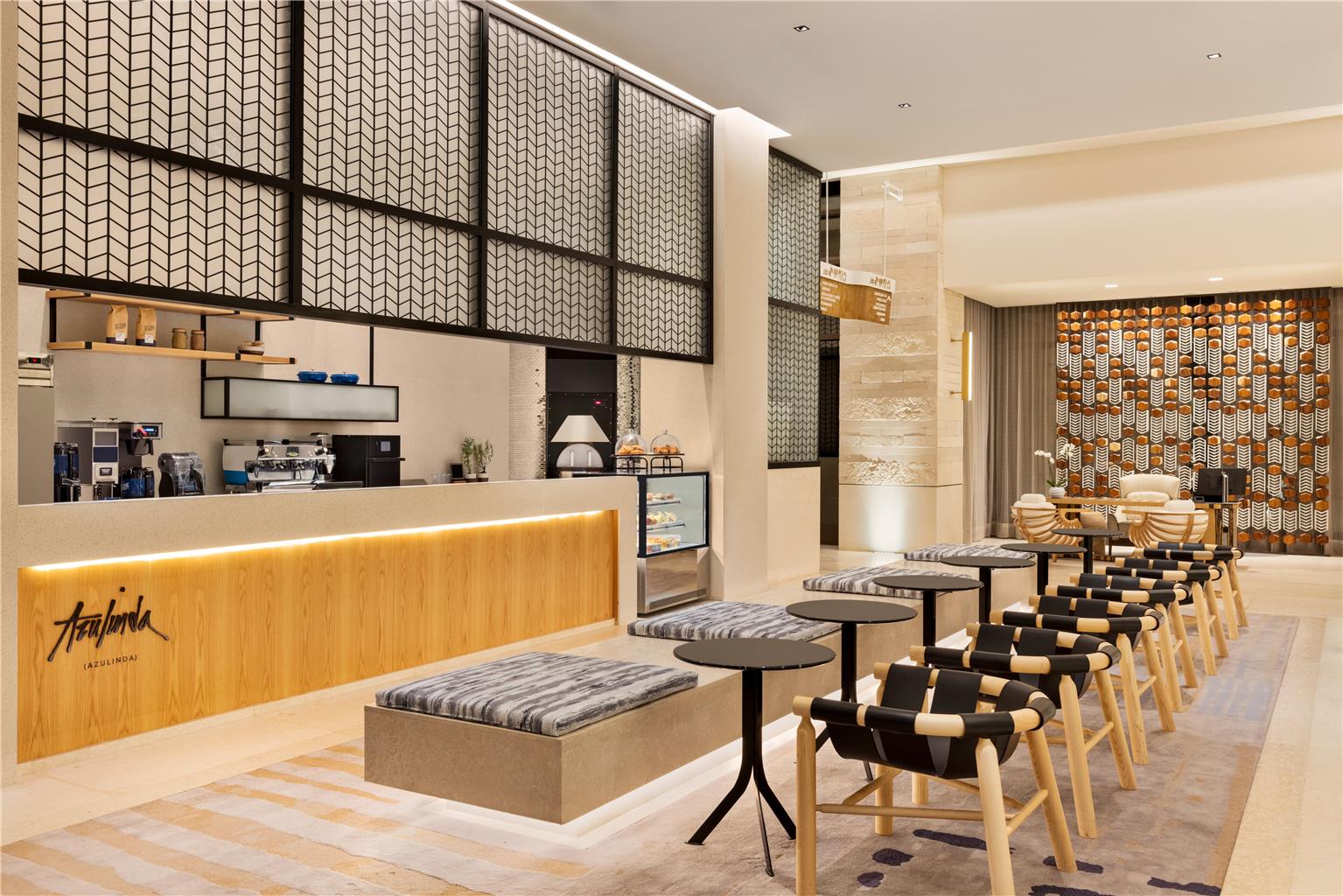 Modern cafe interior at Hilton Cancun with wooden counter, geometric wall panels, and rows of wooden chairs with striped cushions at small tables.