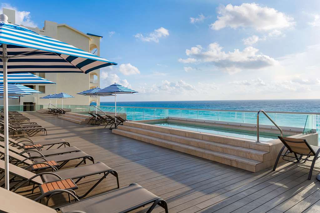 Oceanfront deck at Hilton Cancun Mar Caribe with lounge chairs, blue-striped umbrellas, and an infinity pool overlooking turquoise Caribbean waters.