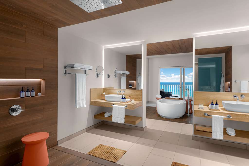 Modern bathroom with dual white vessel sinks, teal accent walls, wood paneling, walk-in shower, and heated towel racks at Hilton Cancun Mar Caribe.