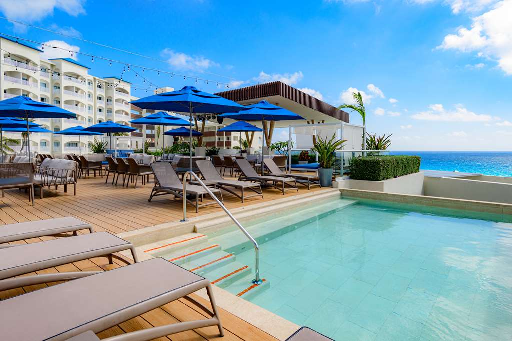 Spacious lobby at Hilton Cancun Mar Caribe with beige flooring, white columns, wooden accents, scattered seating areas, and ocean views through floor-to-ceiling windows.