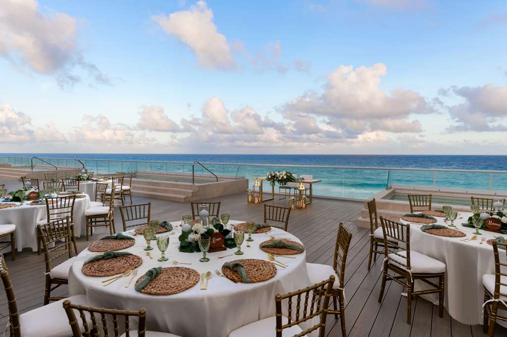 Modern dining room at Hilton Cancun Mar Caribe with wooden lattice ceiling, tables set with place settings, and open kitchen visible behind glass.