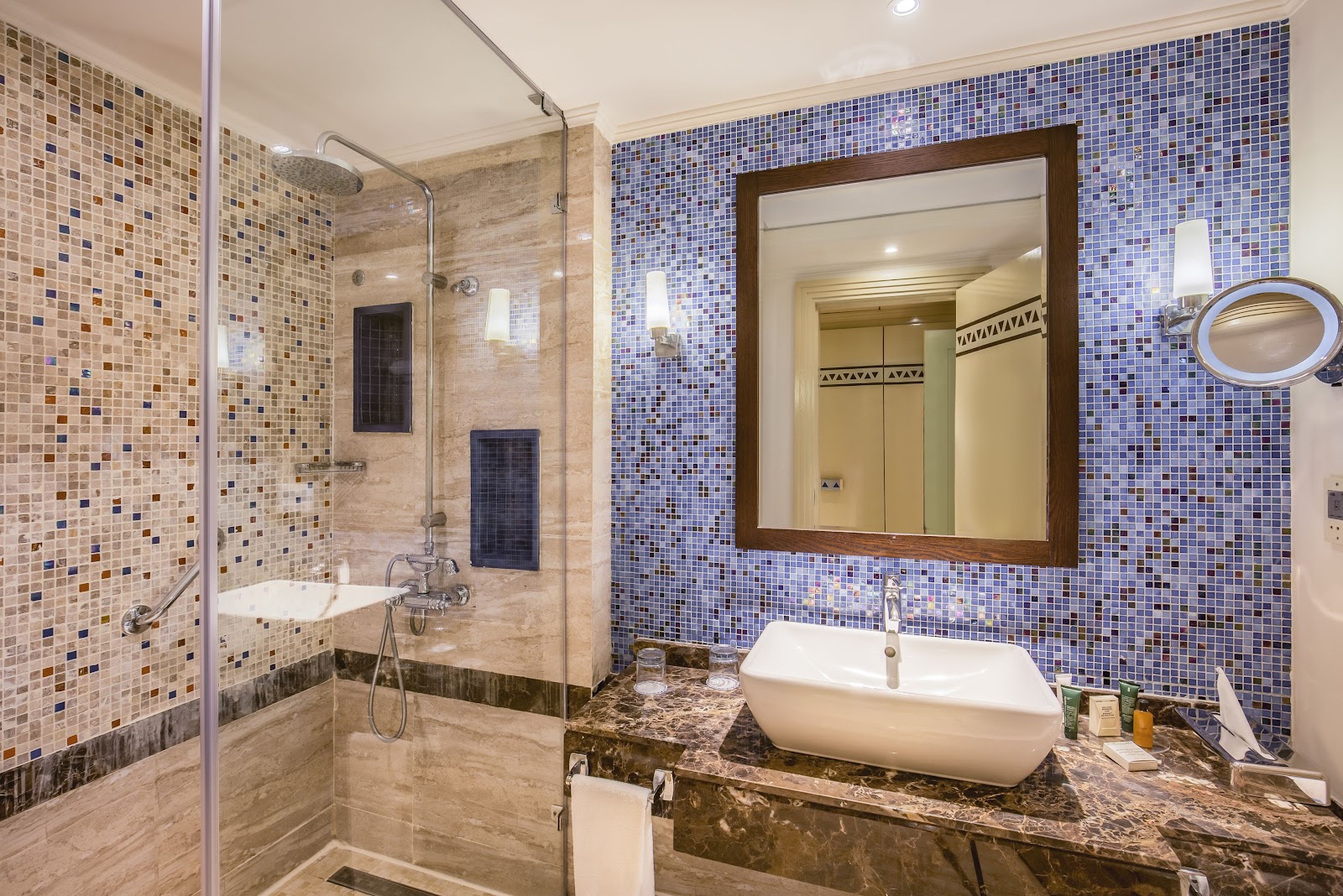 Bathroom with blue mosaic tile walls, marble countertop with vessel sink, large mirror, and walk-in shower with glass enclosure.