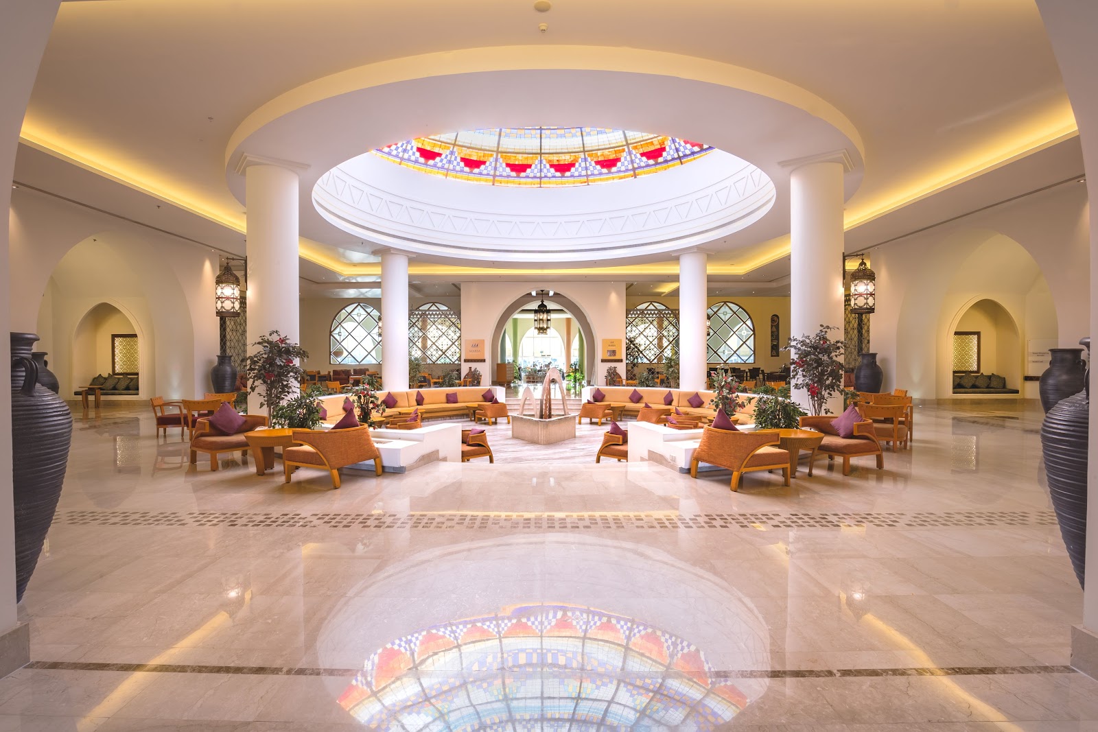 Spacious lobby at Hilton Marsa Alam Nubian Resort with domed skylight, white columns, wooden seating areas, and geometric tile flooring.
