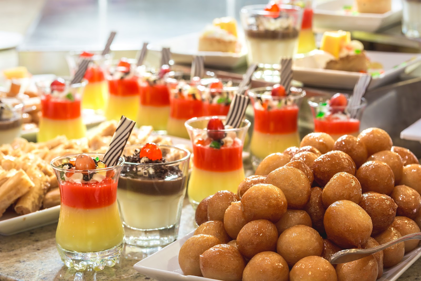 Buffet spread with layered desserts in glasses, fried dough balls, pastries, and small plated sweets at Hilton Marsa Alam Nubian Resort.