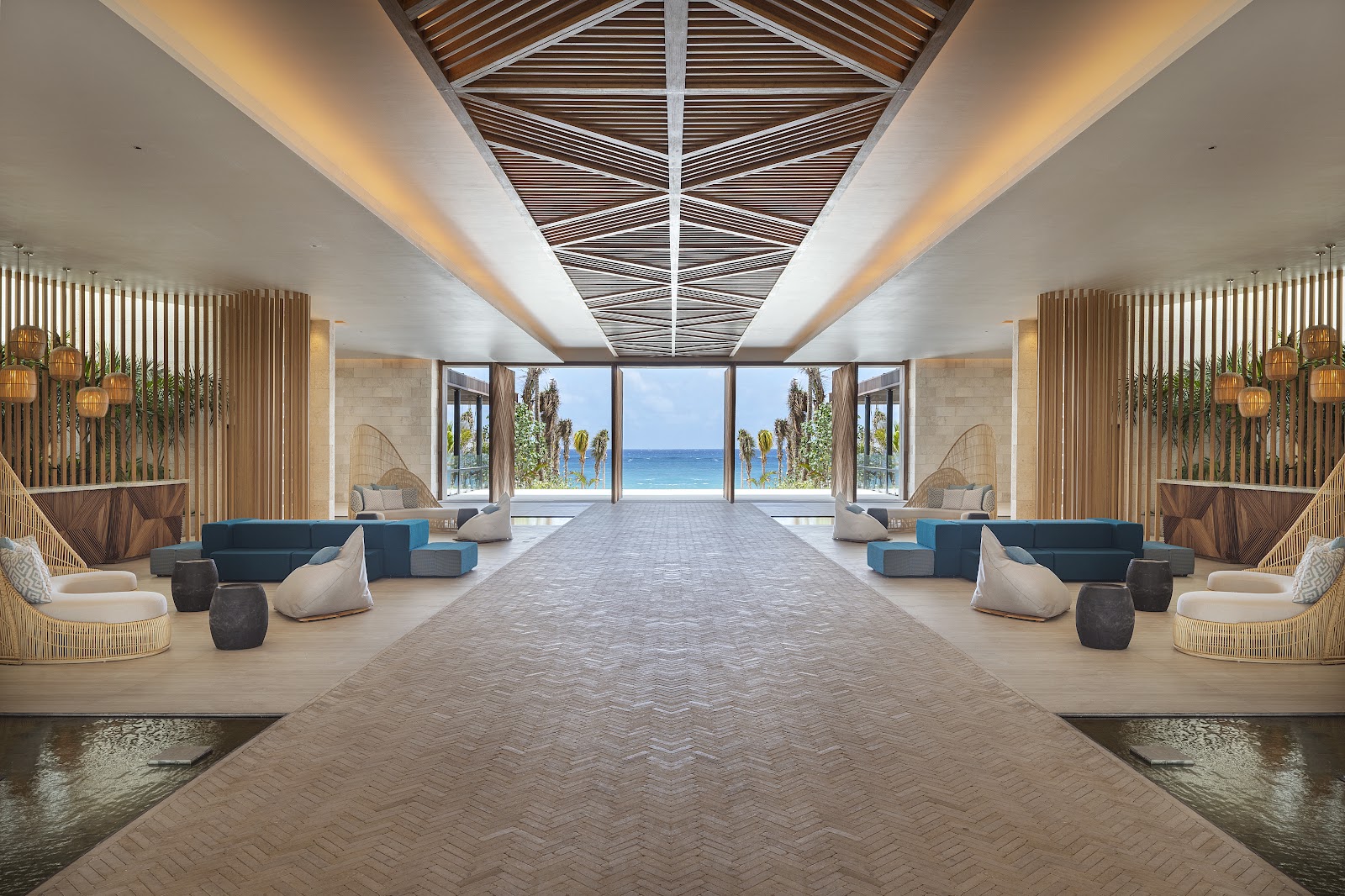 Spacious lobby at Hilton Tulum Riviera Maya with symmetrical seating areas, wooden accents, and ocean views through floor-to-ceiling windows.