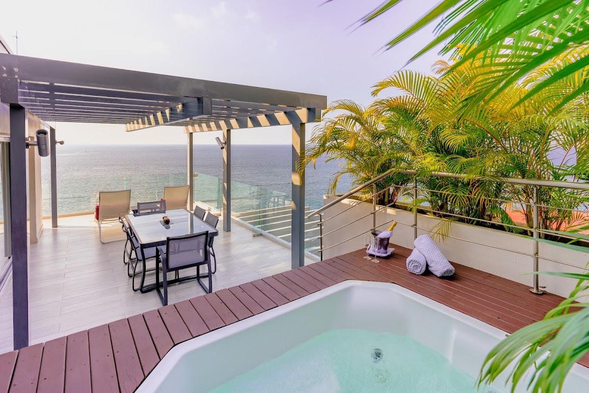 Private oceanview terrace at Hilton Vallarta Riviera with hot tub, dining table, lounge chairs, pergola, and palm trees overlooking the sea.