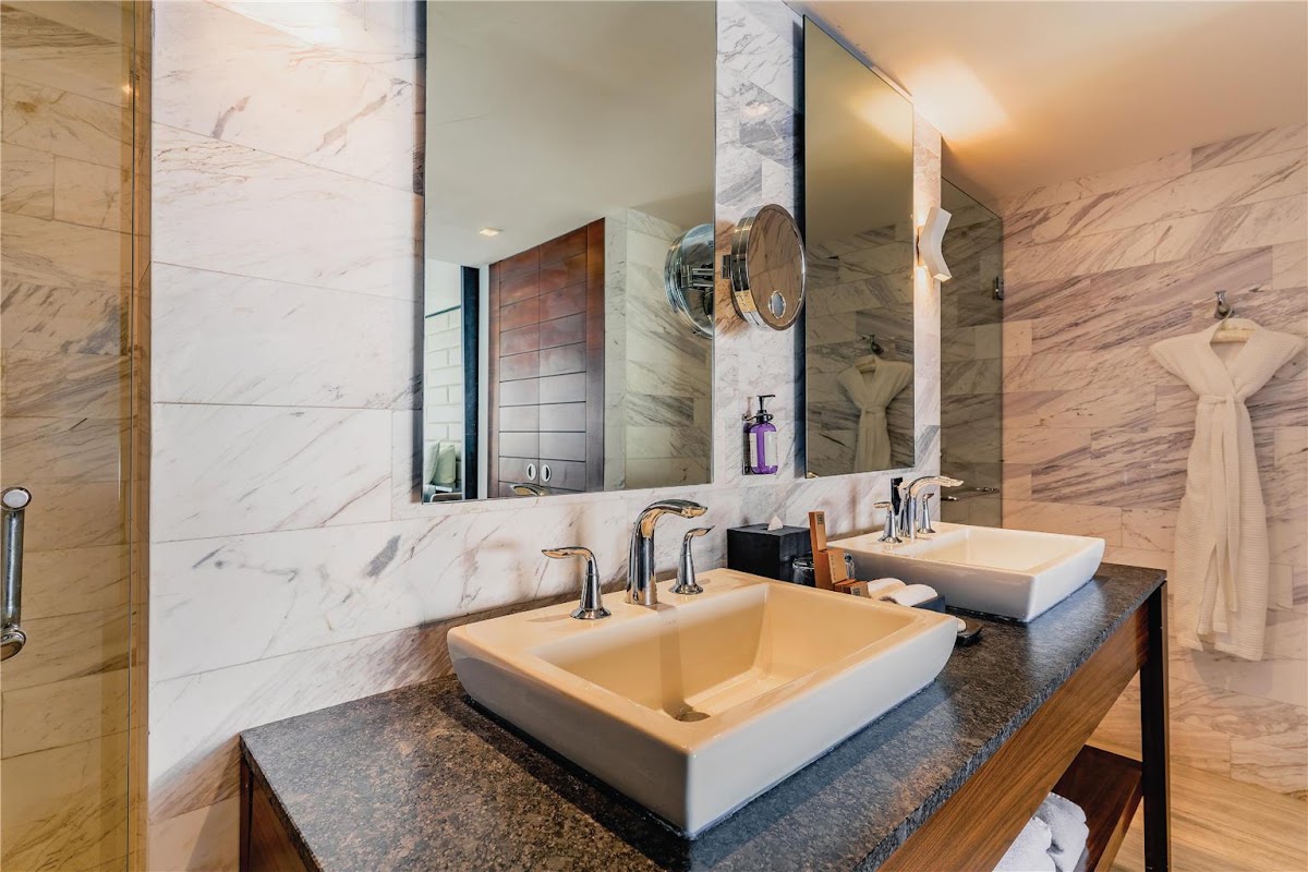 Spa-like bathroom at Hilton Vallarta Riviera with dual vessel sinks, marble walls, and large mirror above dark countertop.