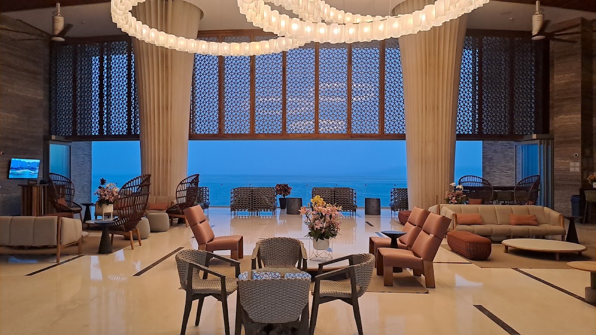 Hilton Vallarta Riviera's modern lobby lounge with woven chairs, coral seating, circular light fixtures, and floor-to-ceiling ocean views at dusk.