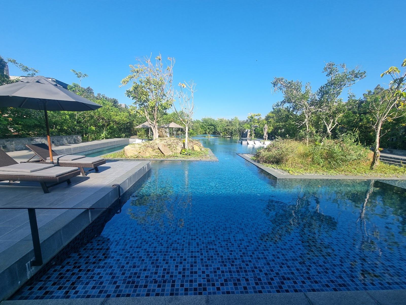 Turquoise pool with white cabana beds surrounded by tropical trees and a modern dark building under blue sky at Hilton Yala Resort.