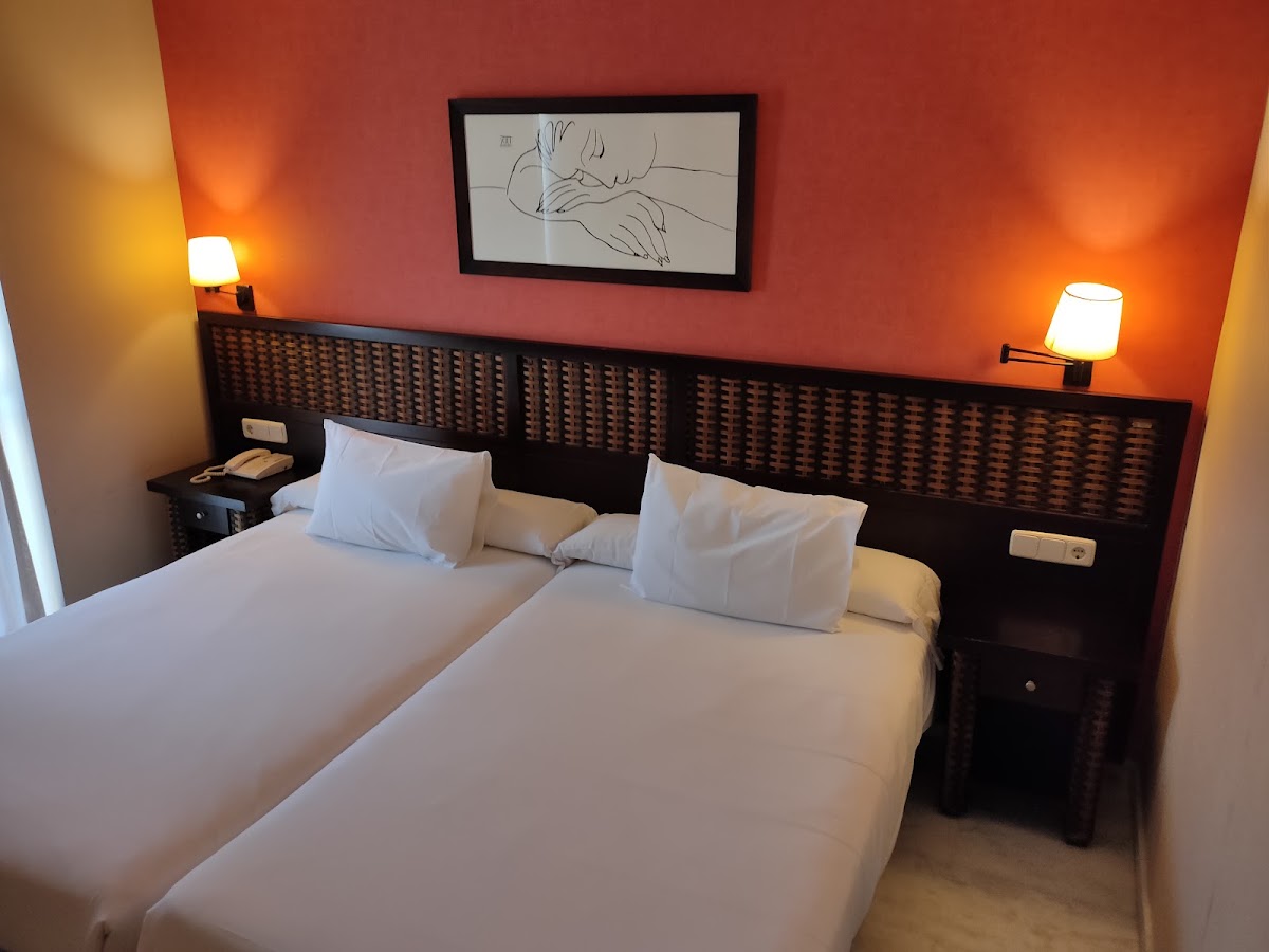 Twin beds with white linens in a resort room with orange walls, dark wood headboard, and framed line drawing above.