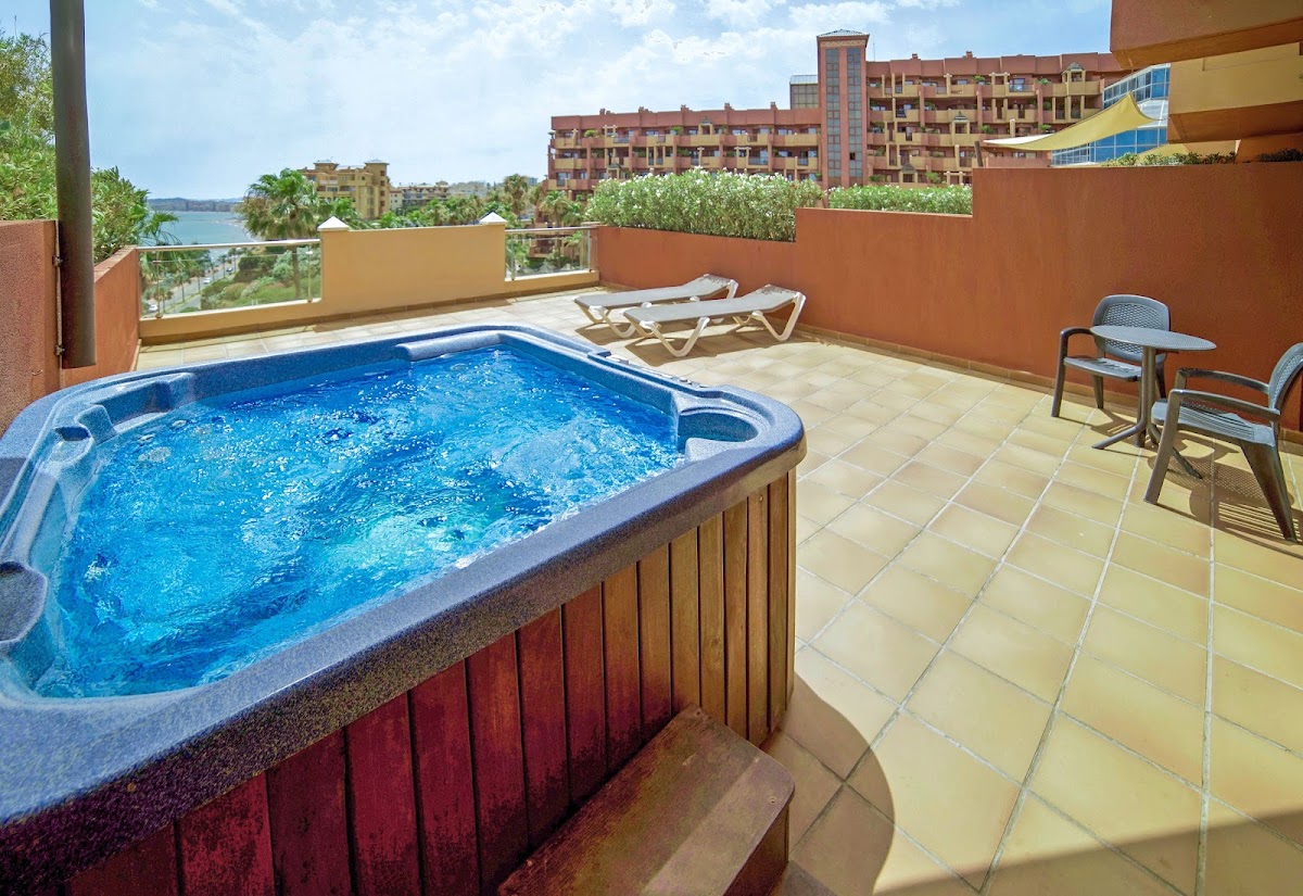 Private terrace with hot tub, lounge chairs, and waterfront view of red resort buildings and lake.