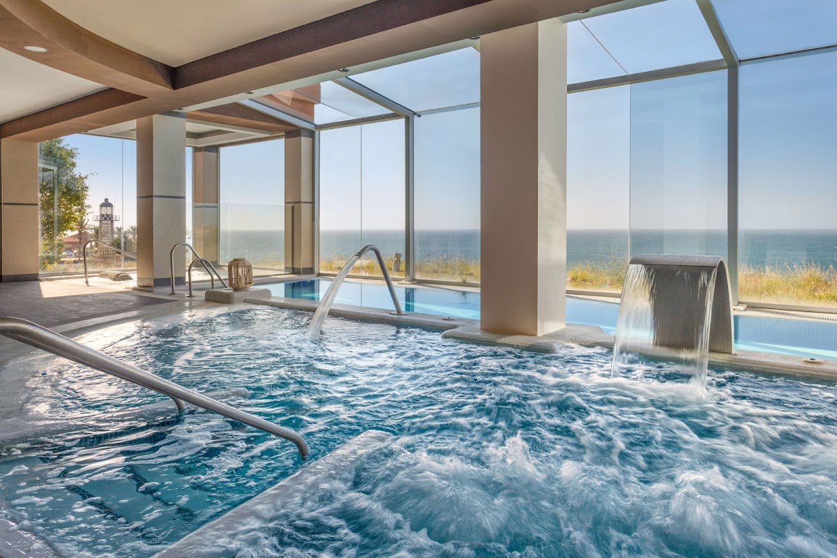 Indoor spa with hot tub, waterfall features, and floor-to-ceiling windows overlooking the ocean and coastline at Holiday World Polynesia.