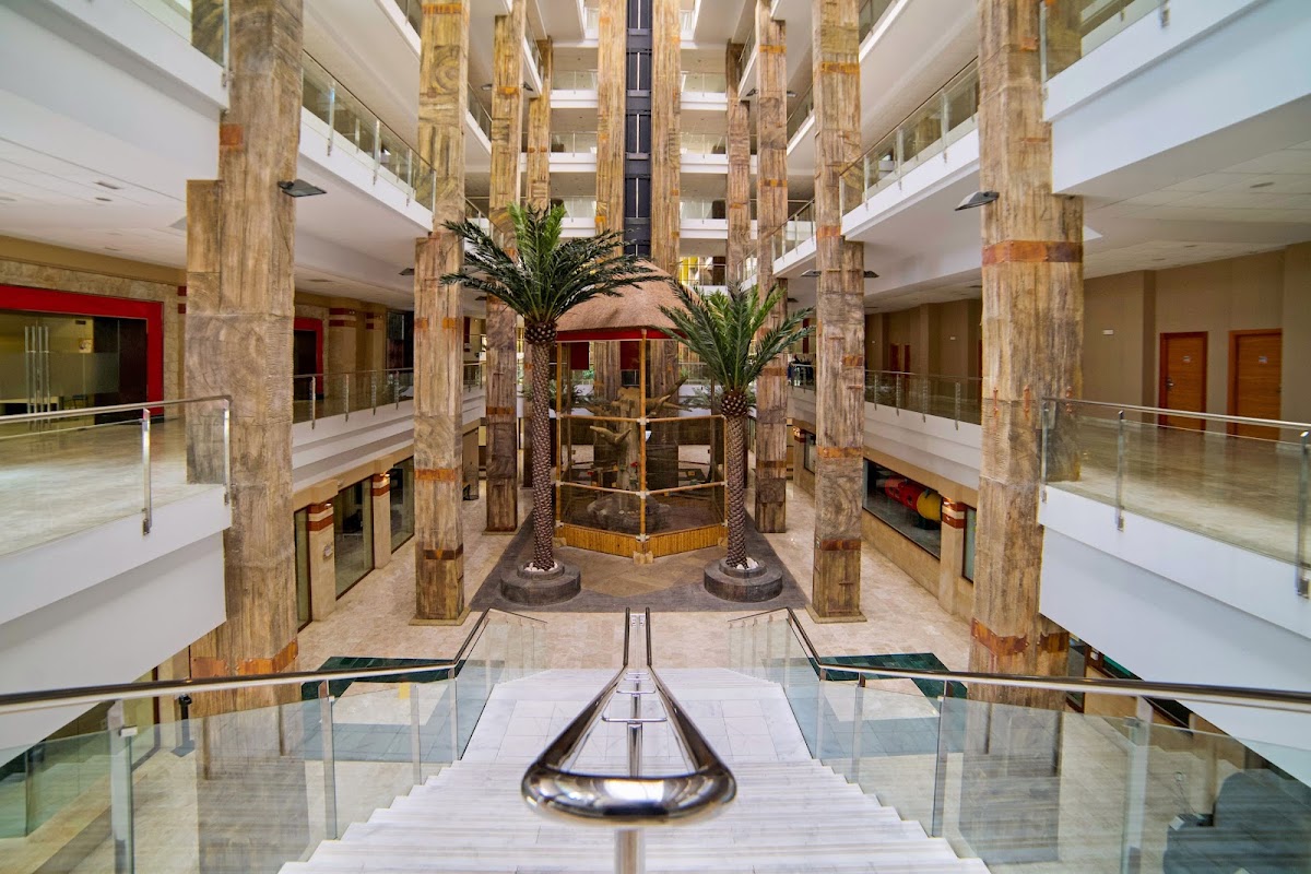 Multi-story atrium with tall marble columns, palm trees, and glass railings overlooking corridors at Holiday World Polynesia.