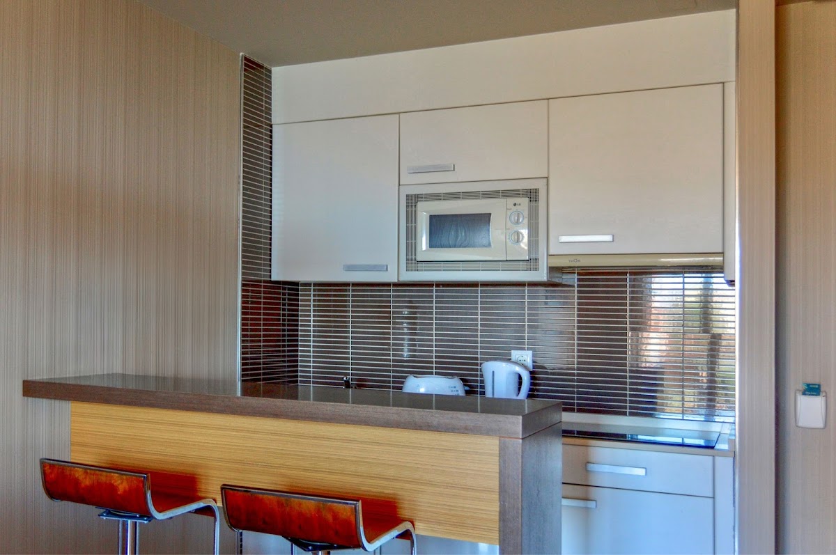 Modern kitchenette with white cabinetry, red tile backsplash, and a counter with red chairs in the foreground at Holiday World Polynesia.