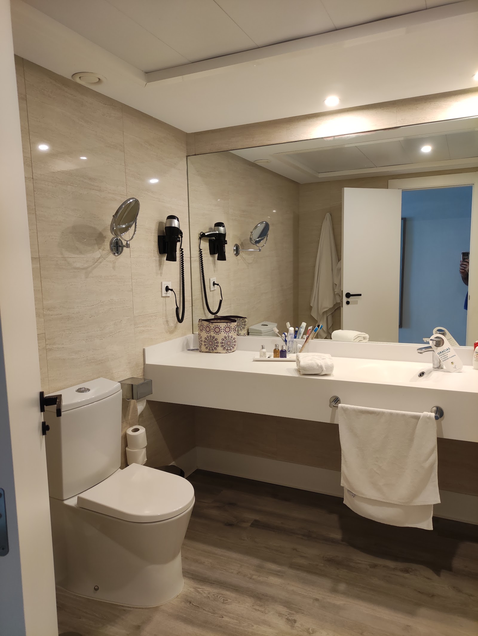 Modern bathroom with white countertop, dual showerheads, large mirror, and beige tile walls with recessed lighting.