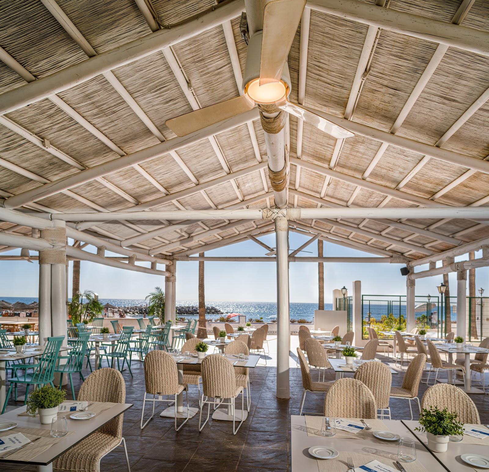 Modern lounge with sculptural pendant lights, woven chairs, and floor-to-ceiling windows overlooking the Mediterranean Sea.
