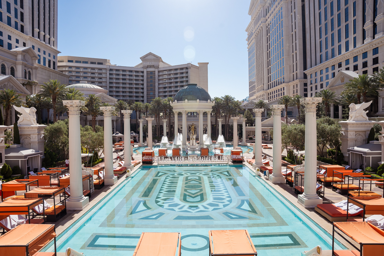Classical columned courtyard with geometric tile pool, orange loungers, and palm trees at Caesars Palace.