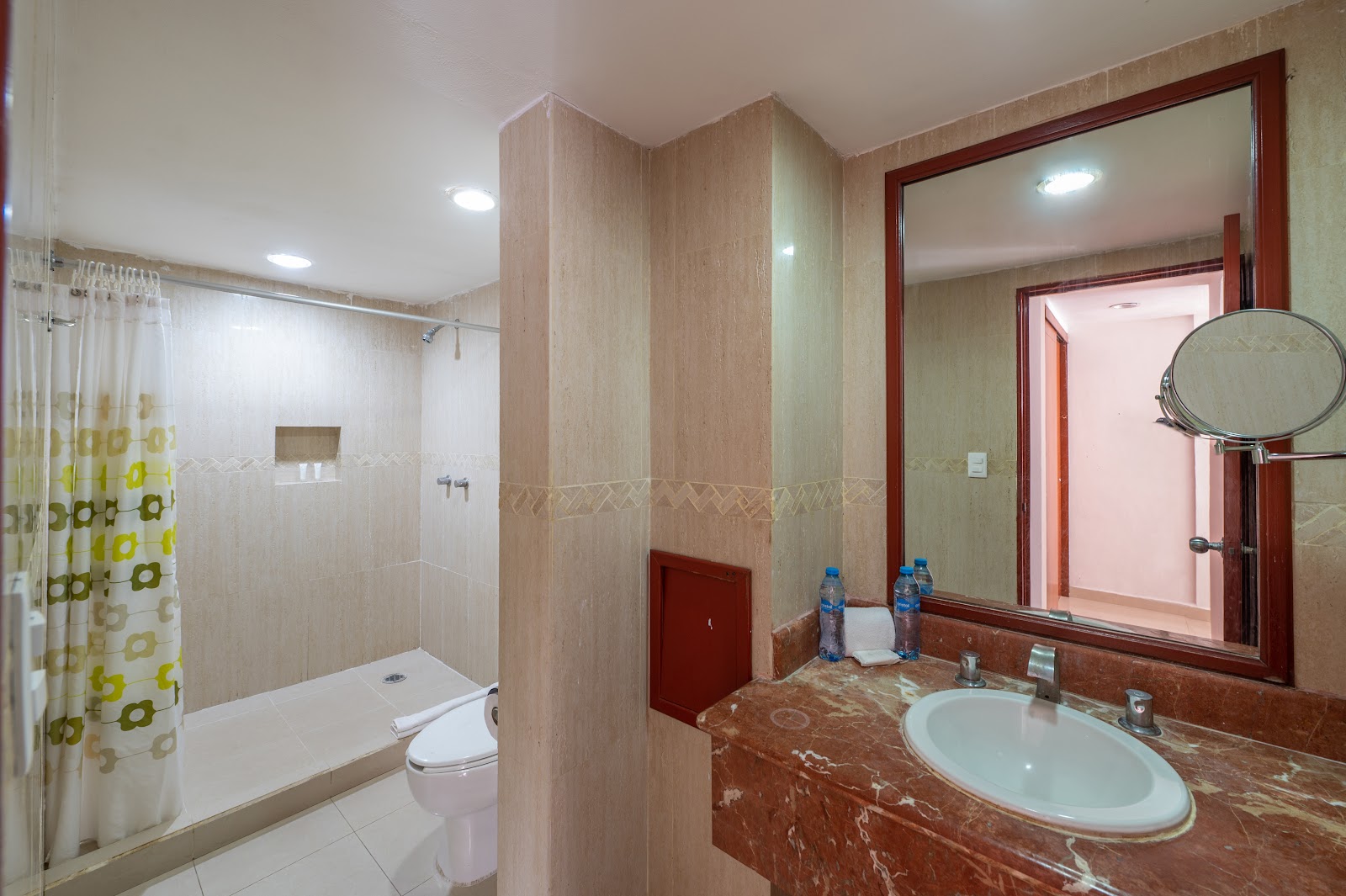 Bathroom with beige tile walls, red-brown marble countertop, round sink, large mirror, shower with curtain, and toilet at Hotel Dos Playas Cancún.