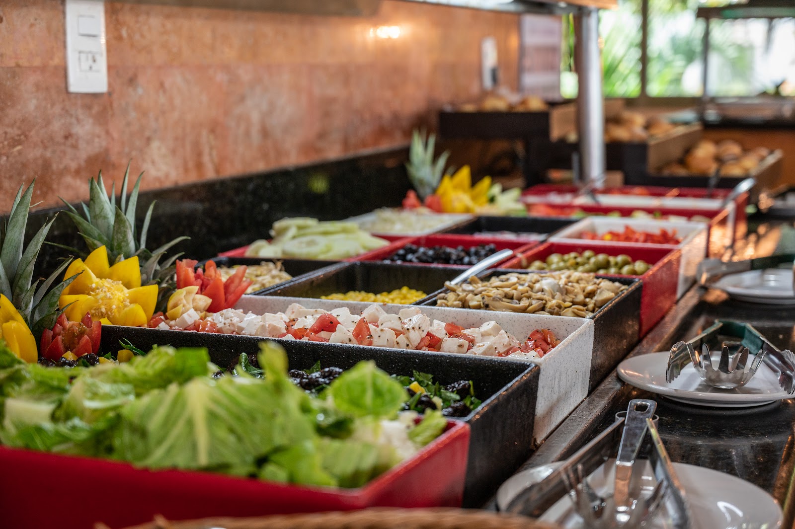 Buffet line at Hotel Dos Playas Cancún displaying fresh salads, vegetables, seafood, and garnishes in red and black serving trays.