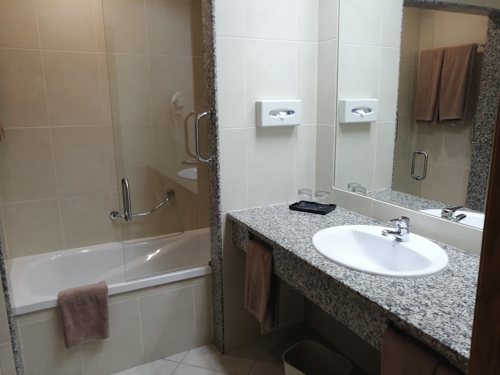 Hotel Guarana bathroom with granite vanity, oval sink, glass shower enclosure with tub, and brown towels on rails.