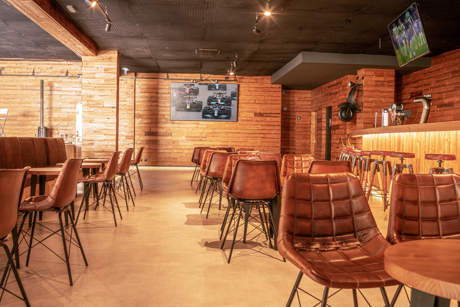 Modern bar and lounge with wood paneling, brown leather chairs, high-top tables, and a wall-mounted TV at Hotel Guarana.