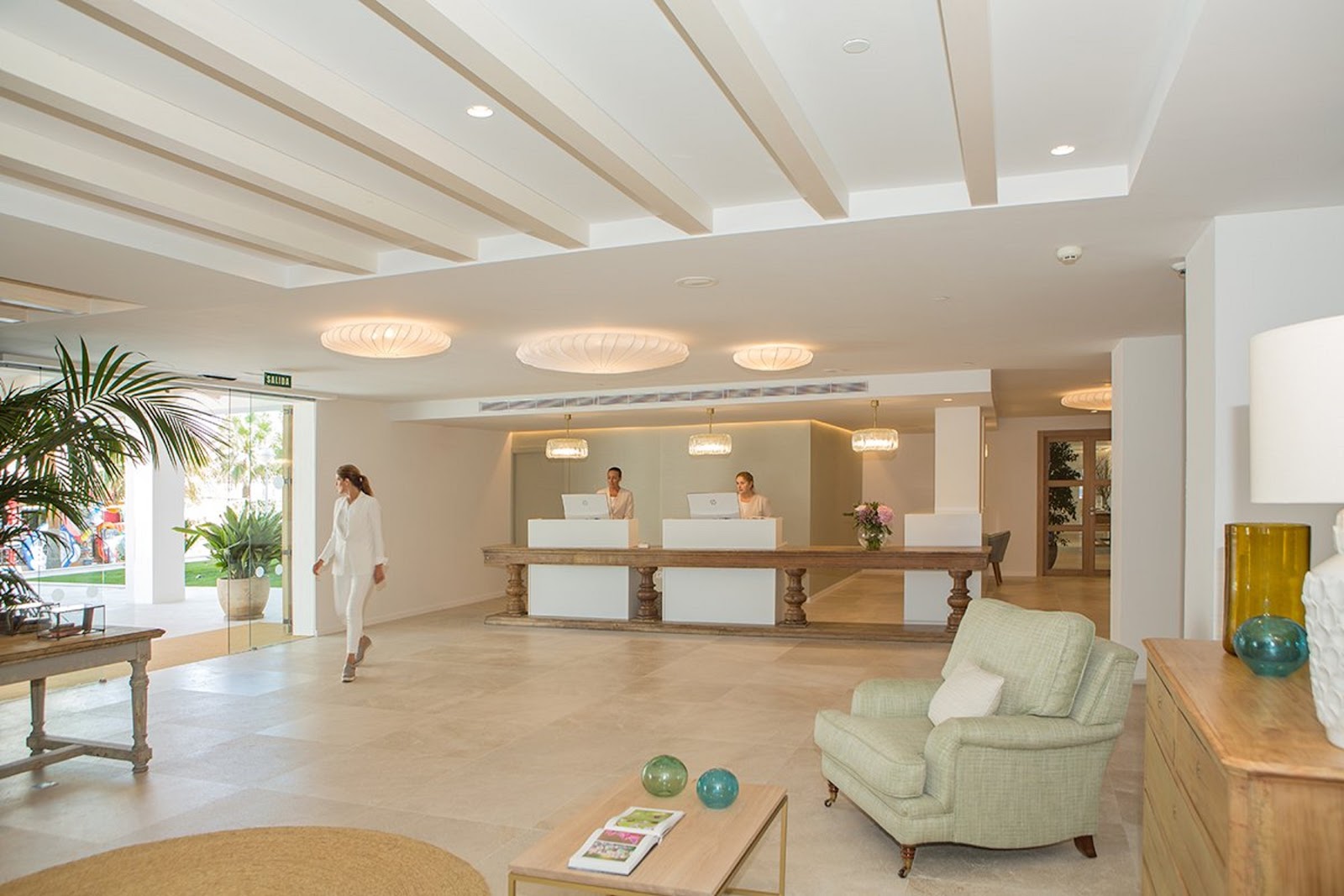 Hotel MySeaHouse Flamingo lobby with beamed ceiling, reception desk with two staff members, seating area with cream armchairs, and tropical plants.