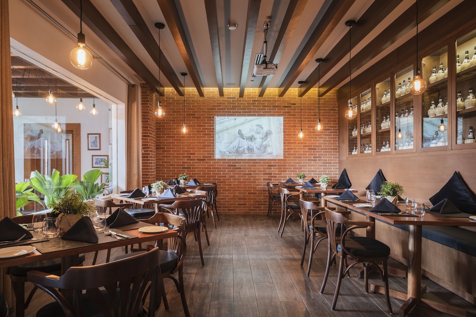 Fine dining restaurant with exposed brick walls, wooden beams, pendant lighting, and place settings with black napkins at Hotel NYX Cancun.