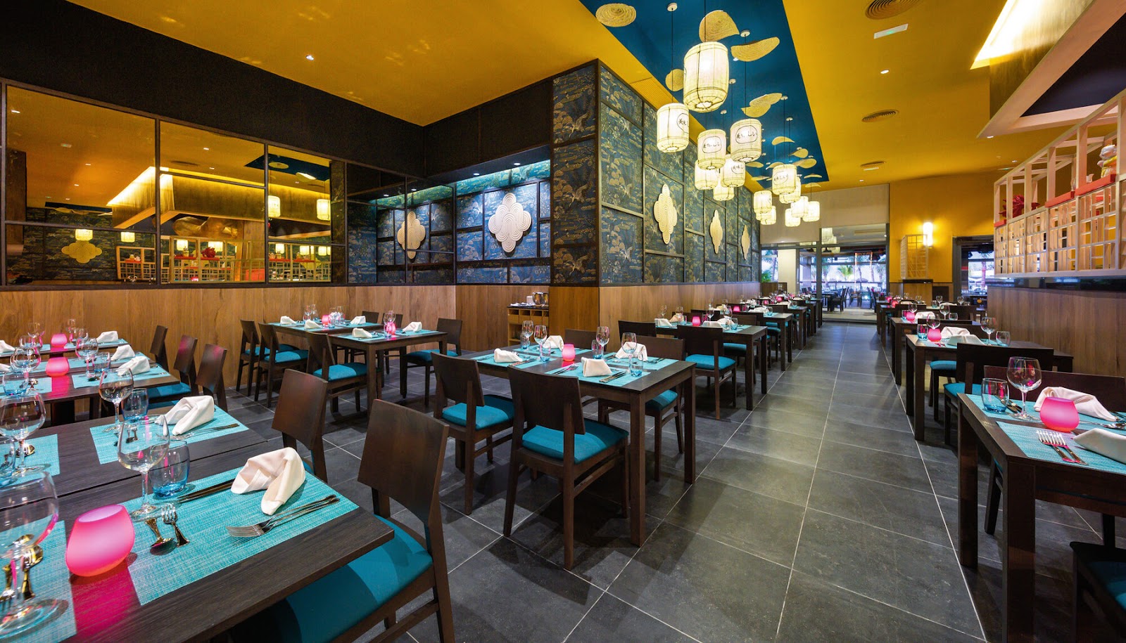 Dining room at Hotel Riu Montego Bay with turquoise and pink table settings, dark wood chairs, and gold and blue ceiling details.