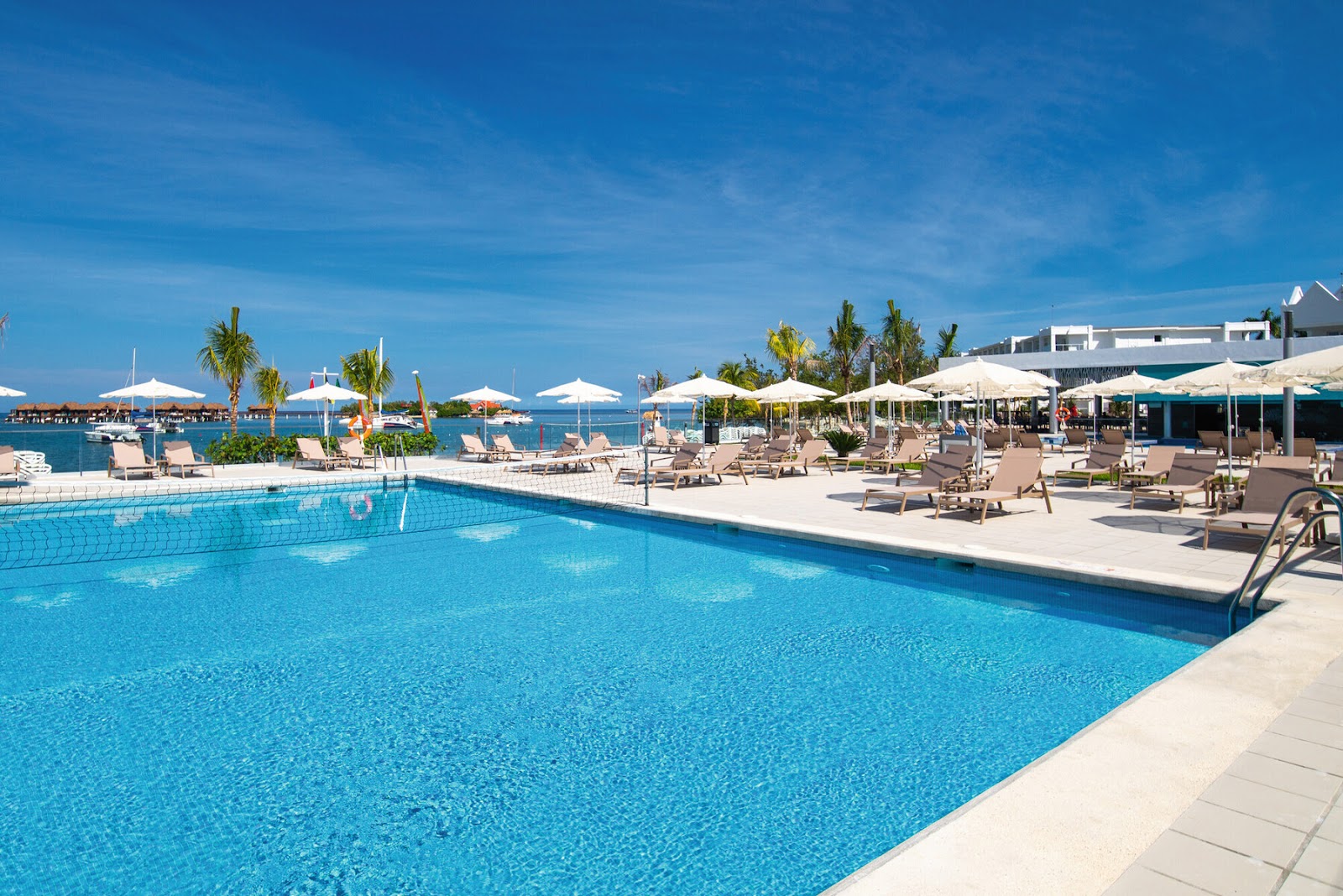 Resort pool with lounge chairs and white umbrellas, overlooking the Caribbean Sea and palm trees at Hotel Riu Montego Bay.