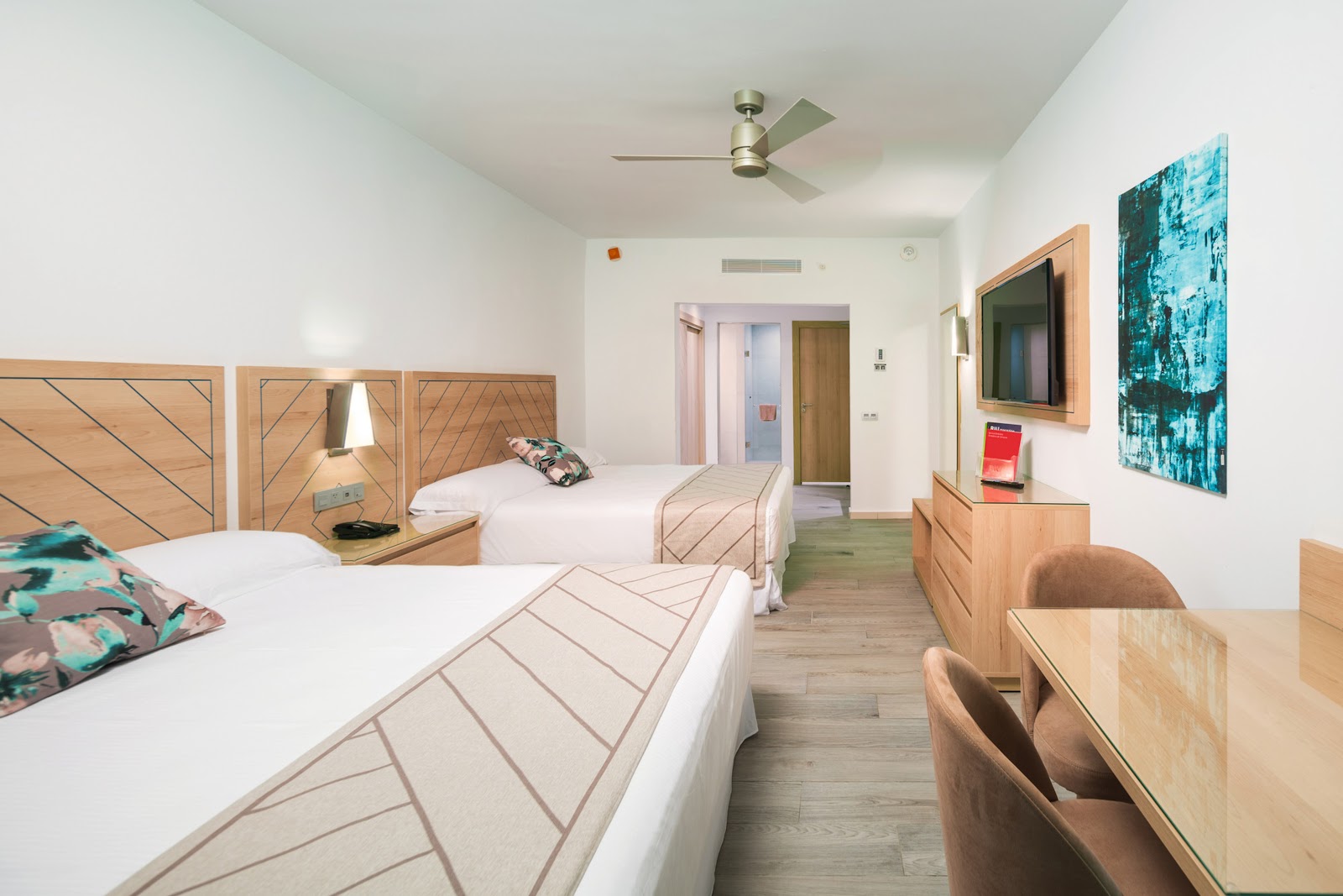 Hotel Riu Ocho Rios guest room with two queen beds, wooden furniture, wall-mounted TV, and bathroom entrance.