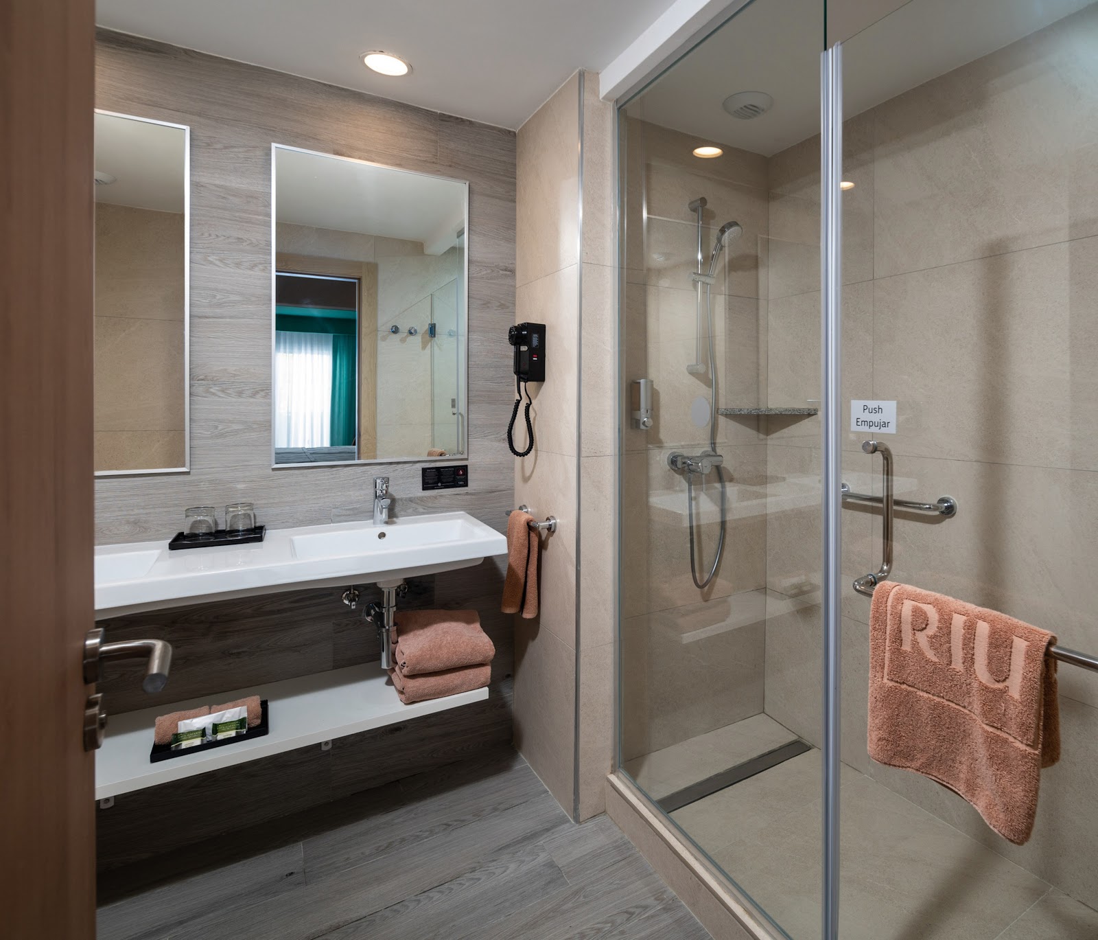 Modern bathroom with double sink vanity, lighted mirrors, and glass-enclosed shower with coral towels at Hotel Riu Ocho Rios.
