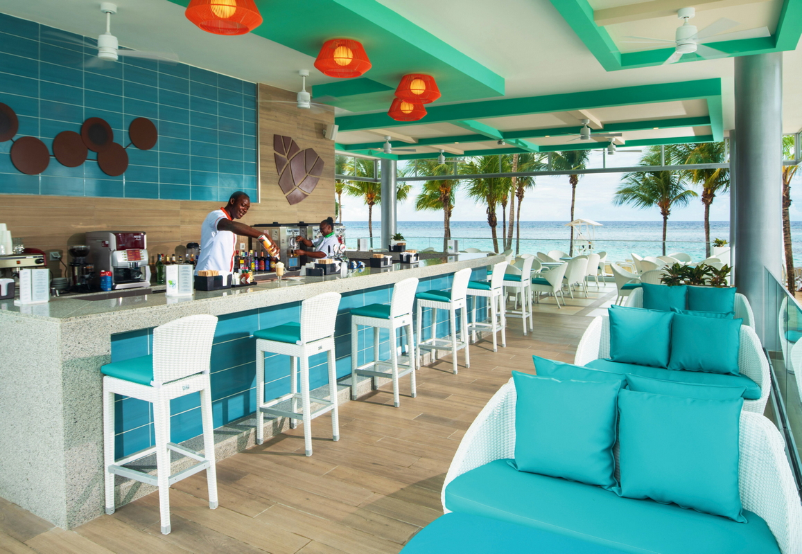 Bar area with turquoise and white seating, red lanterns overhead, and ocean view beyond palm trees at Hotel Riu Ocho Rios.