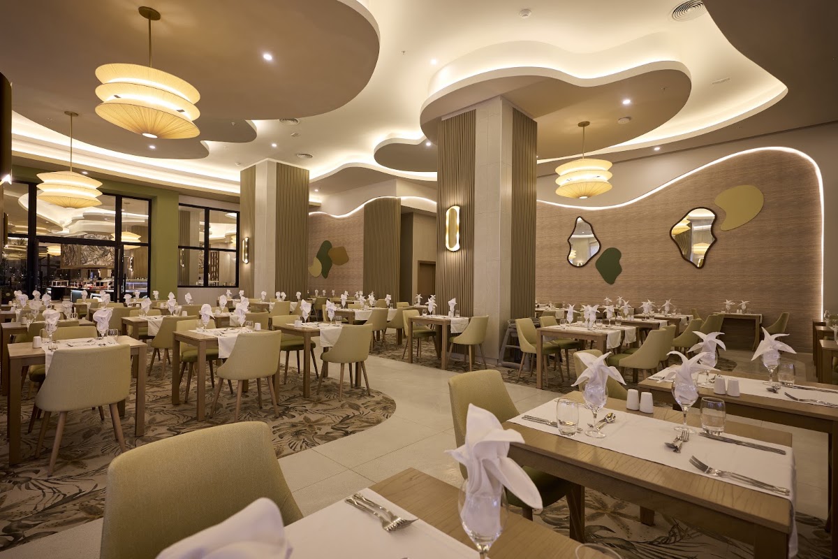 Dining room with sage green chairs, white napkins, and place settings under curved beige ceiling with pendant lights and decorative mirrors.