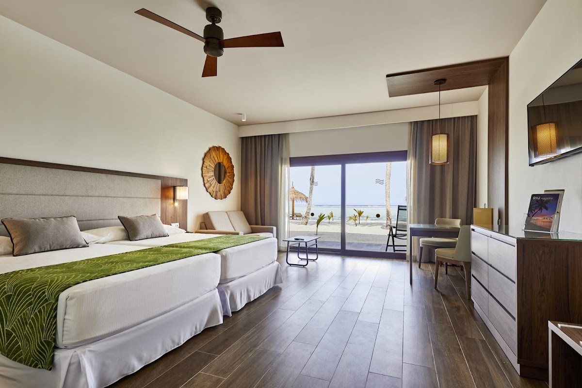 Double beds with green accents in a resort room with ocean and palm tree views through sliding glass doors.