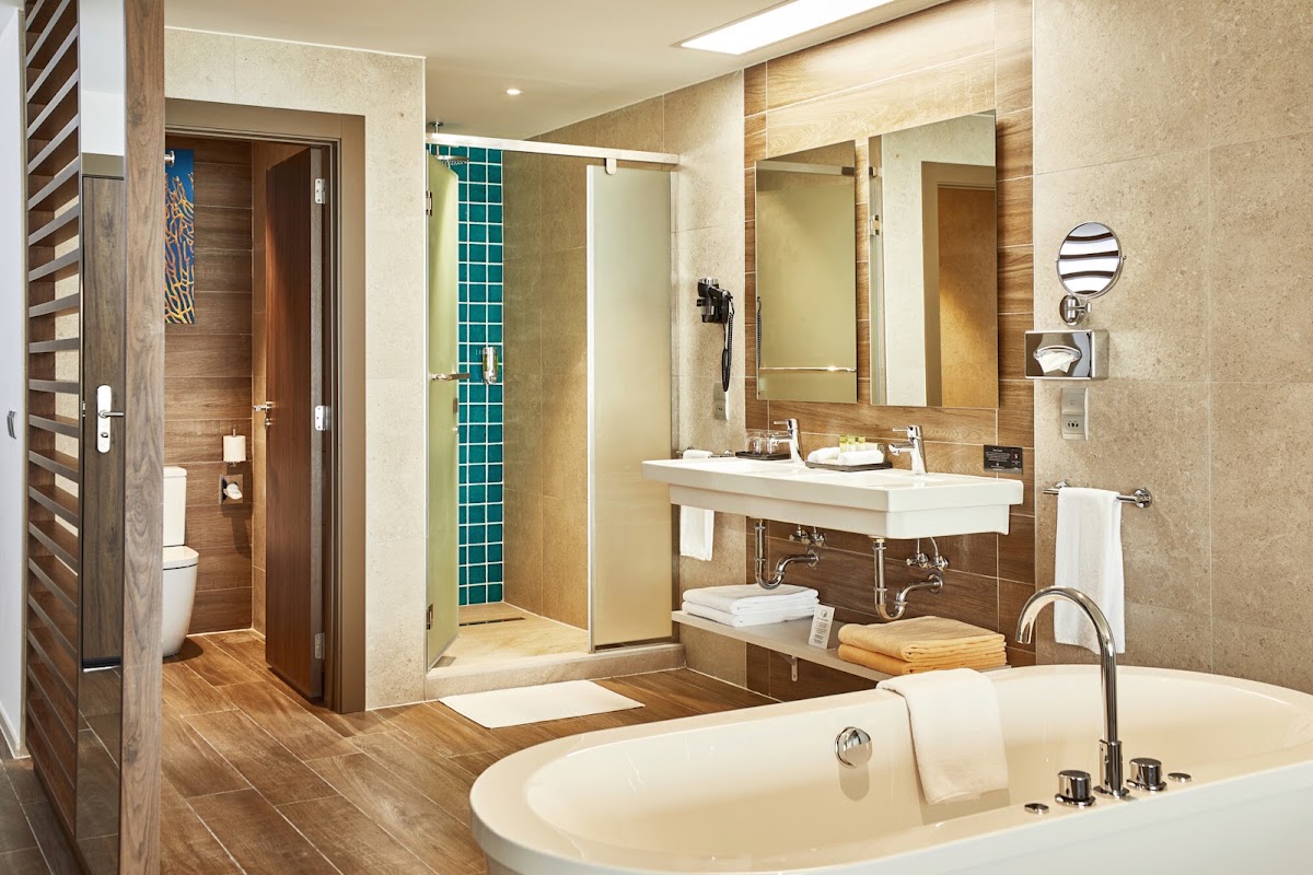 Spacious bathroom with soaking tub, double vanity sink, glass-enclosed shower with teal tile accent, and wood flooring throughout.