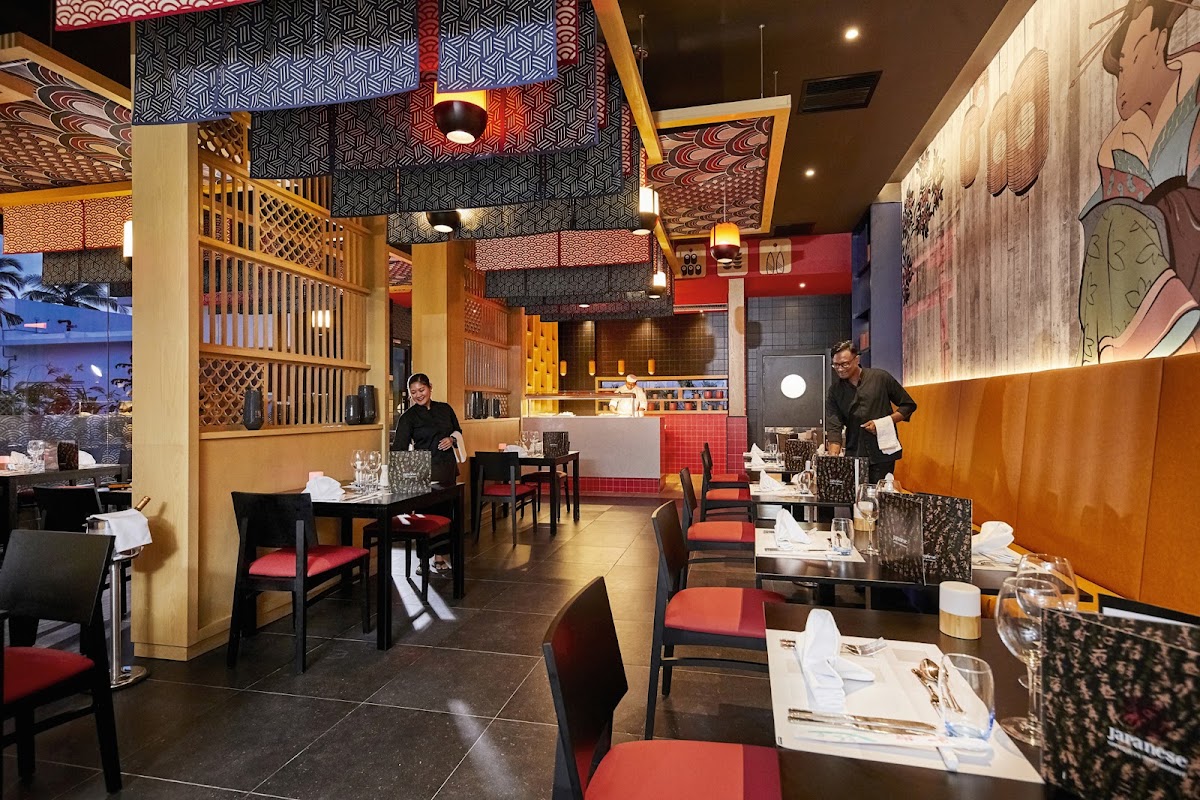 Modern restaurant interior at Hotel Riu Palace Maldivas with black chairs, red cushions, geometric patterned ceiling, and staff attending to tables.