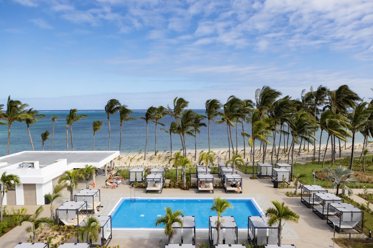 Aerial view of Hotel Riu Palace Mauritius pool overlooking the beach, turquoise ocean, and palm trees lining the shore.