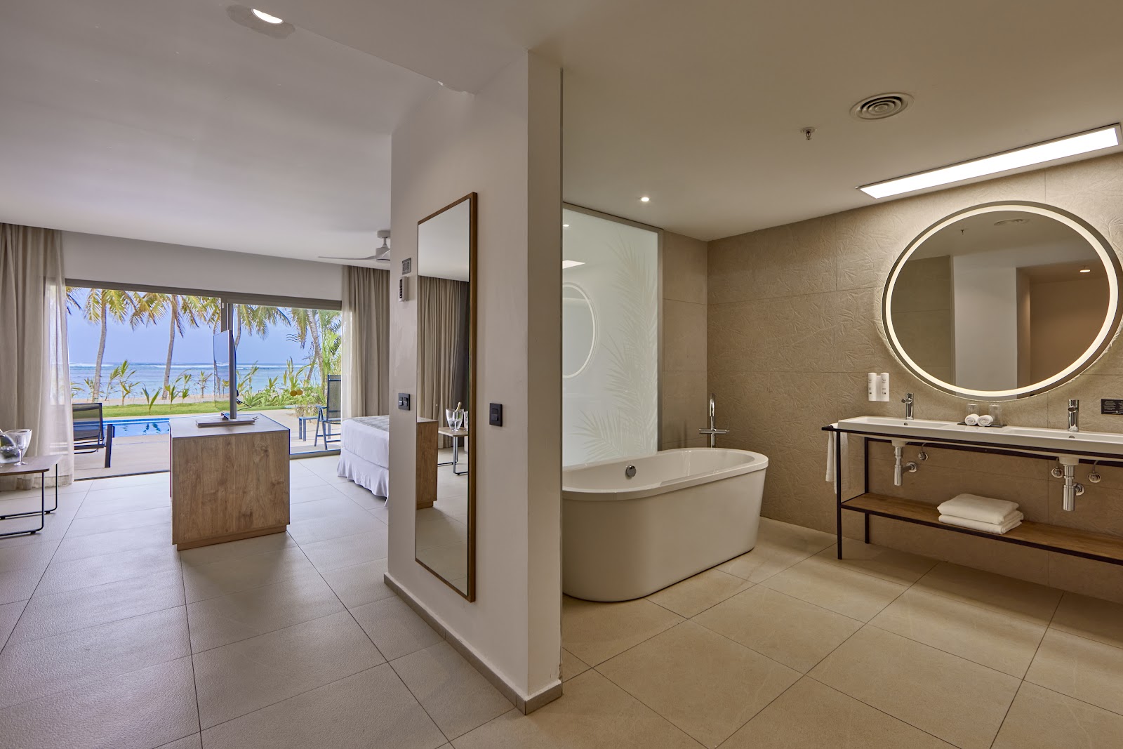 Modern bathroom with oval soaking tub, illuminated mirror, and ocean view through adjoining bedroom at Hotel Riu Palace Mauritius.