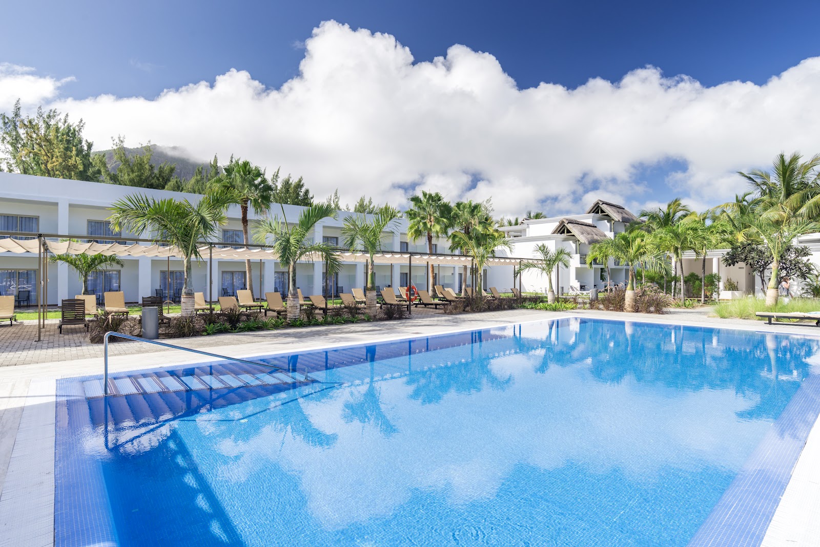 Lush tropical grounds with palm trees, manicured lawns, a blue pool, and beach beyond at Hotel Riu Palace Mauritius.