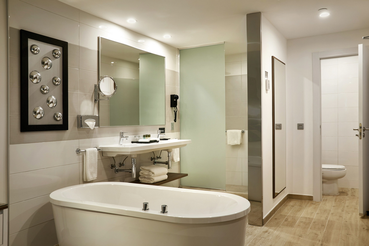 Resort bathroom with freestanding soaking tub, floating vanity with green-tiled shower enclosure, and decorative wall art.