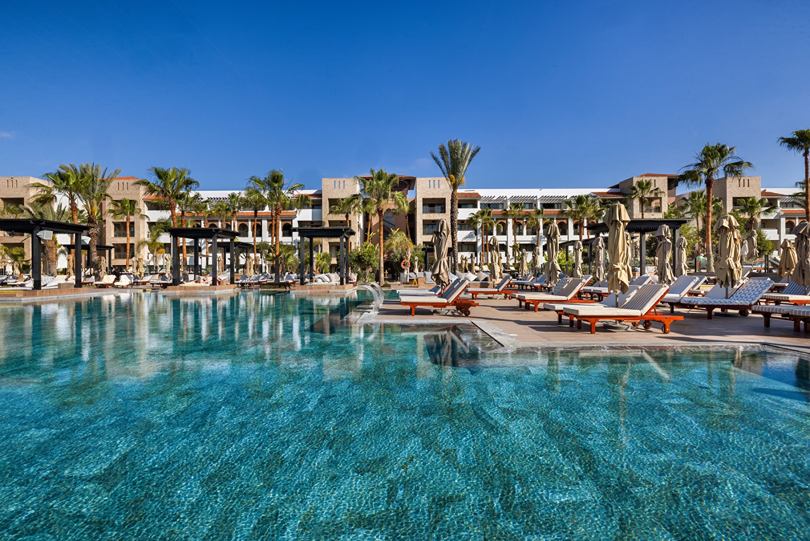 Covered lounge area with pink cushioned seating, striped columns, and ocean view at Hotel Riu Palace Tikida Agadir.
