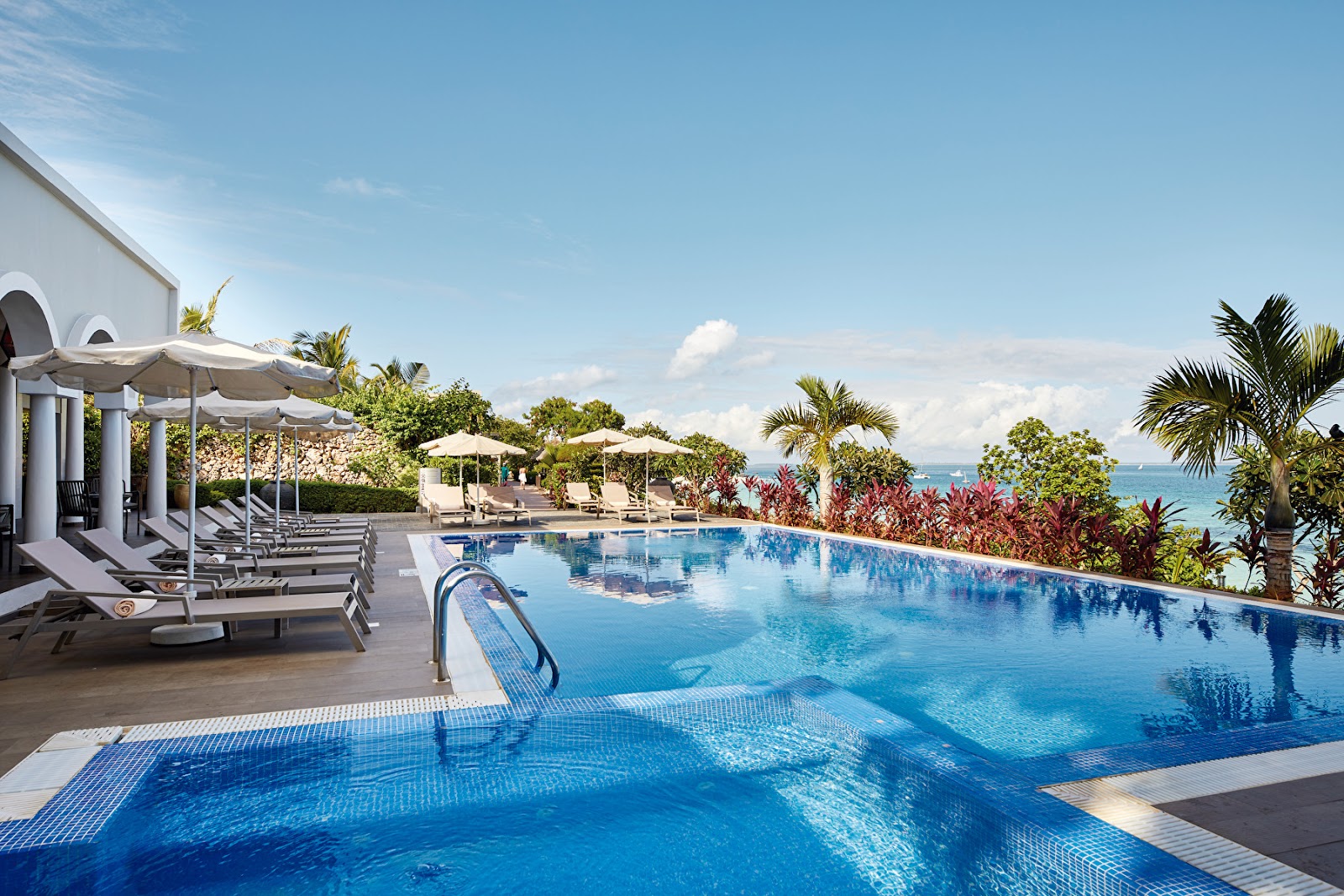 Infinity pool overlooking the ocean at Hotel Riu Palace Zanzibar, with loungers, umbrellas, and tropical vegetation along the coastline.