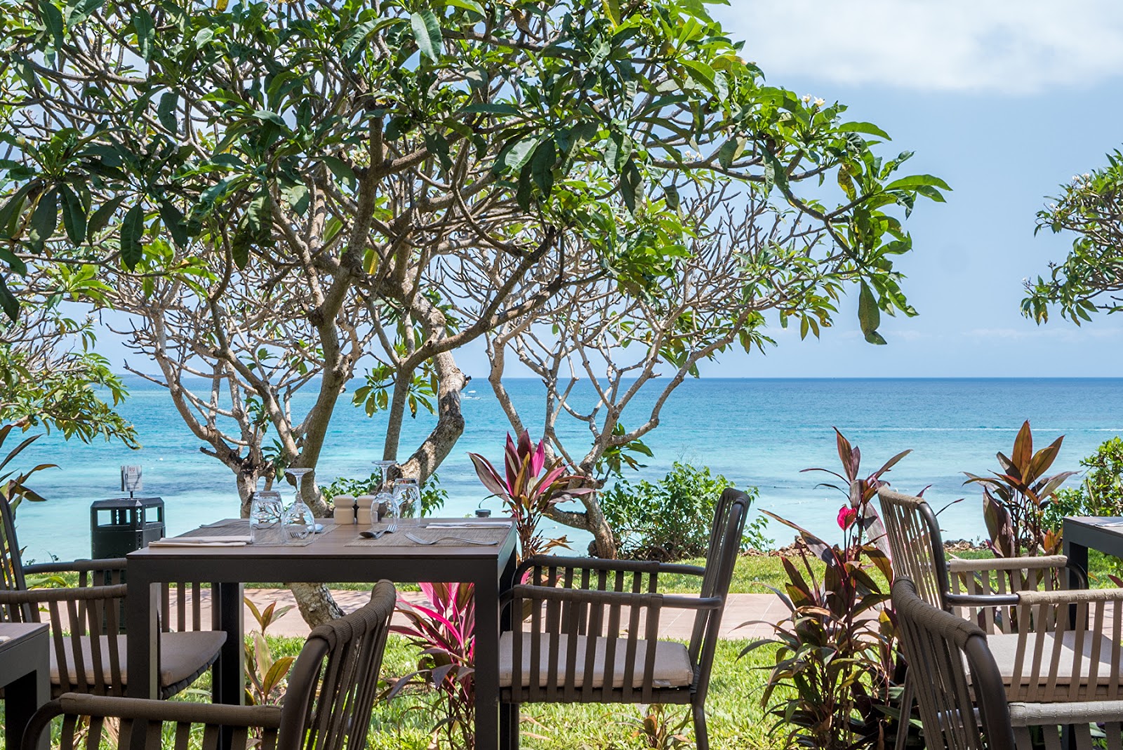 Spacious resort suite with four-poster canopy bed, sitting area, desk, and ocean view from balcony doors at Hotel Riu Palace Zanzibar.
