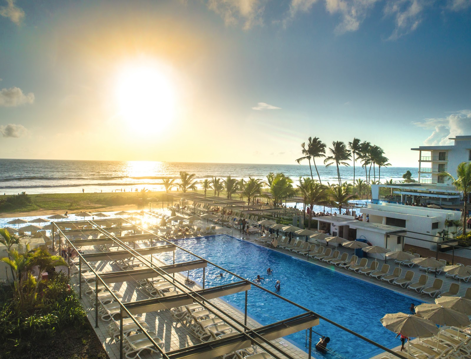 Resort pools and beach with palm trees and ocean at sunrise at Hotel Riu Sri Lanka.