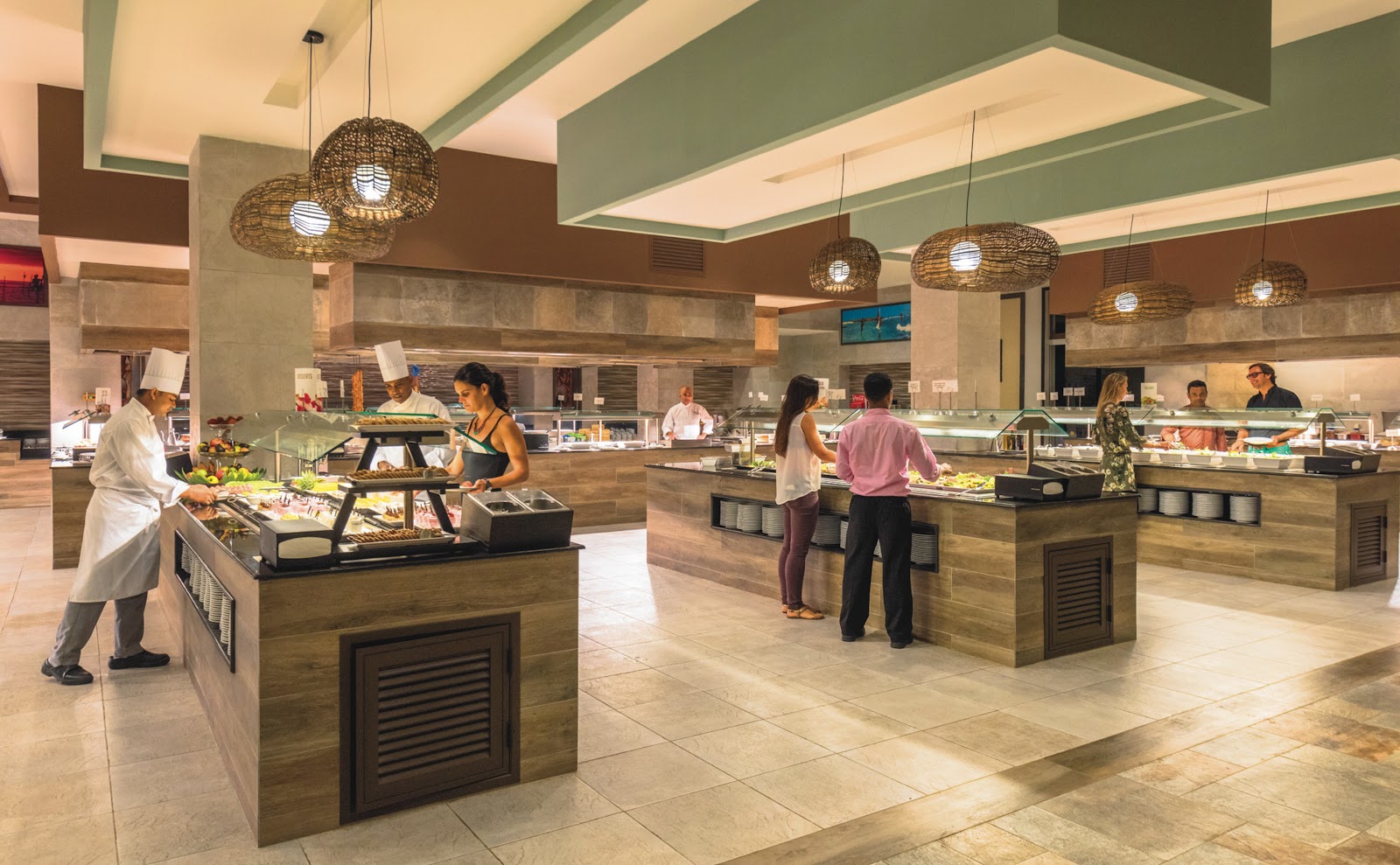 Lobby seating area with bright blue modular sofa, woven chairs, white fluted columns, and geometric blue ceiling with hanging pendant lights.