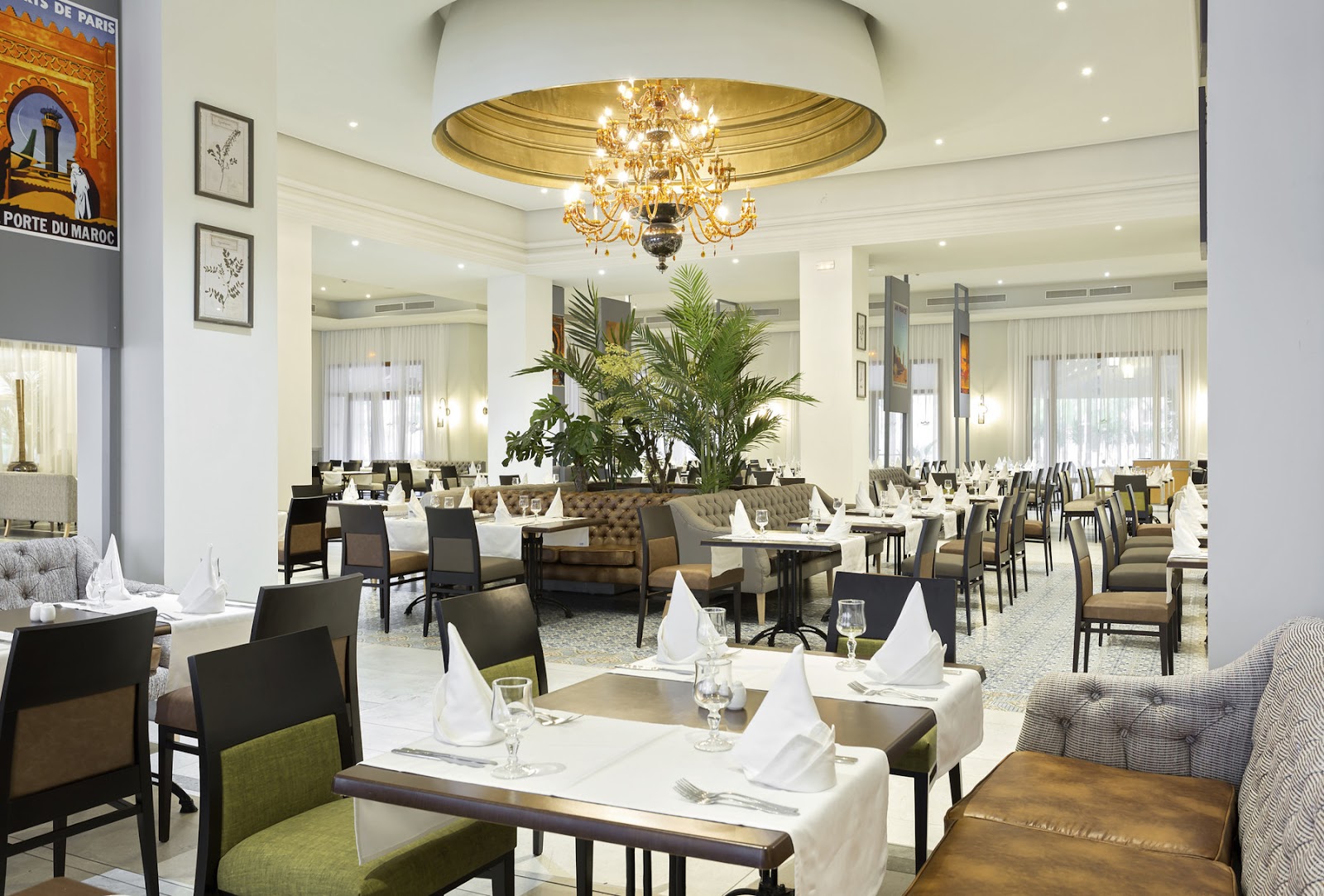 Modern resort buffet kitchen with patterned tile counters, open cooking stations, suspended glass pendant lights, and chefs preparing food behind glass partitions.