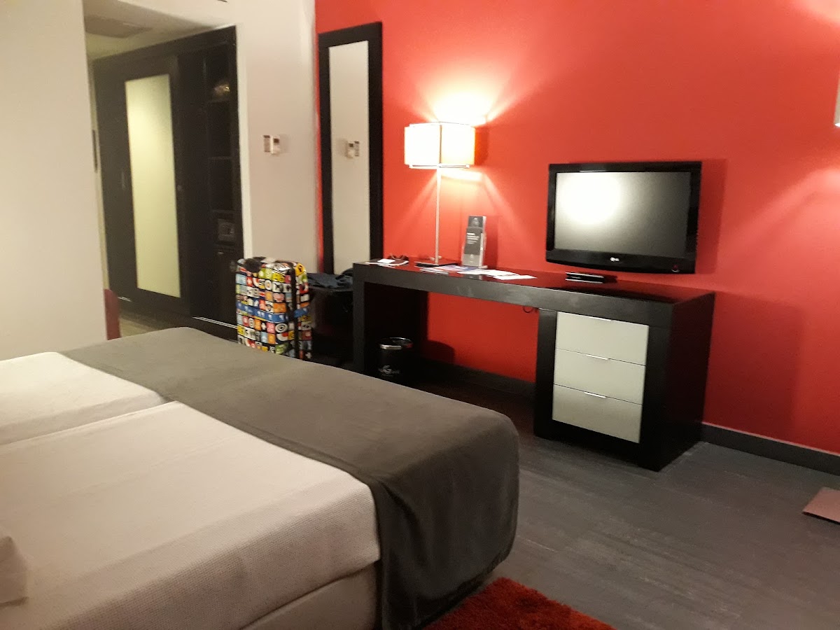 Resort room with bright red accent wall, black entertainment desk with flat-screen TV, and white bedding in foreground.