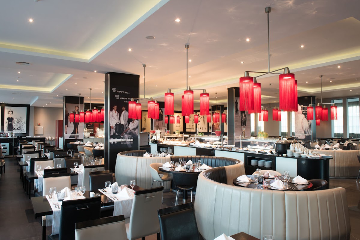 Modern dining room with curved cream banquettes, black tables set with white linens, and numerous red cylindrical pendant lights hanging from a coffered ceiling at Hotel Vila Galé Lagos.