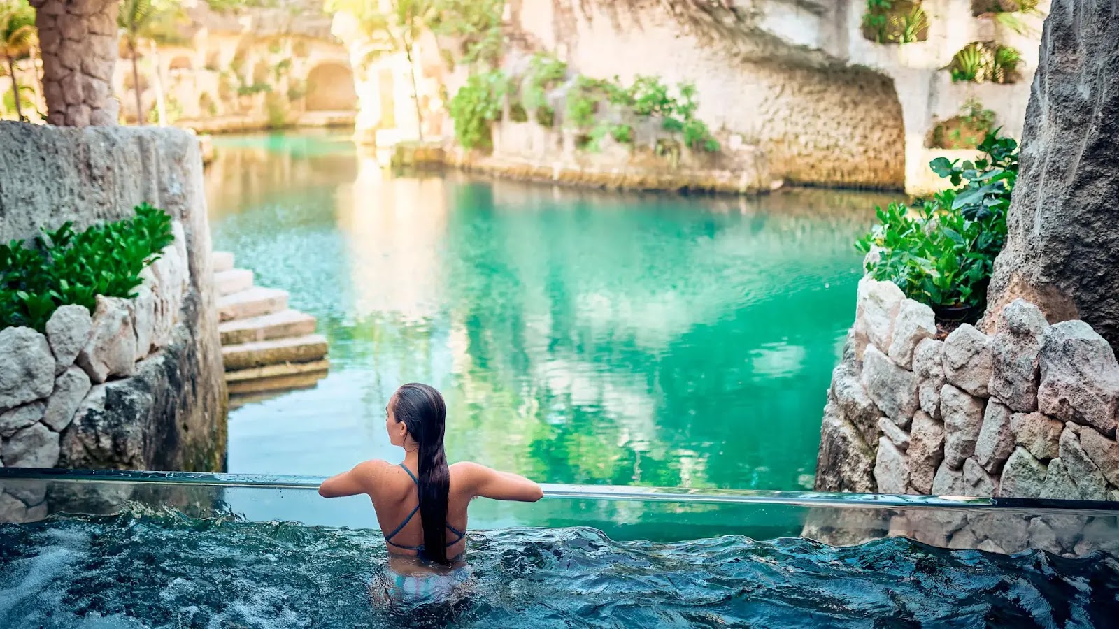Aerial view of Hotel Xcaret Arte with turquoise pools, lagoons, multi-story buildings, and lush vegetation surrounding a beachfront property in Mexico.
